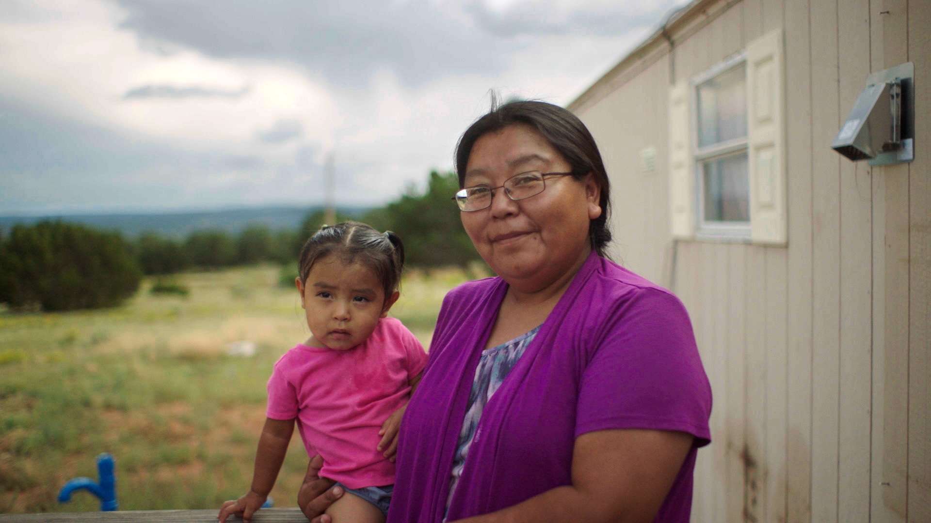 A Native American woman holding a child in her arm looks at the camera.