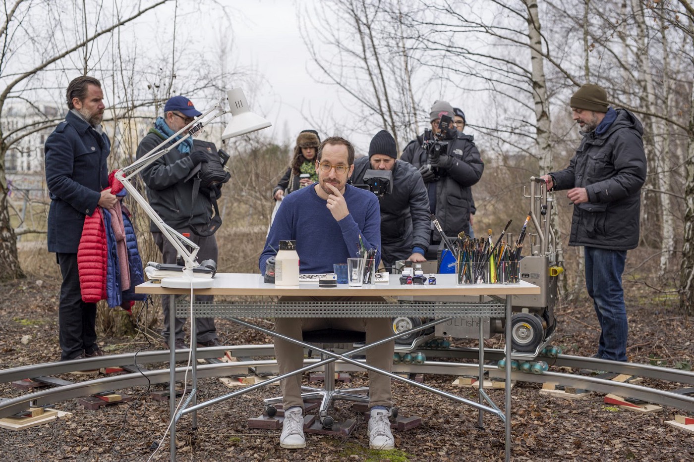 Christoph Niemann sits at a drawing desk in a Berlin park with a film crew setting up behind him.