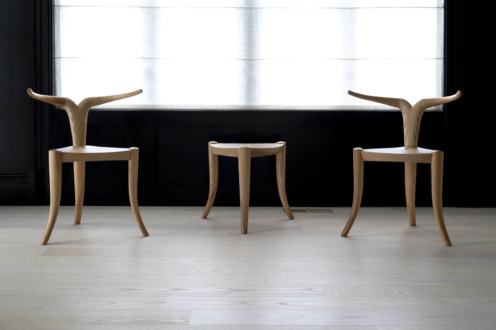 Two 3-legged chairs with antler-like backs and a 3-legged stool of the same height with no back. All in natural white wood.