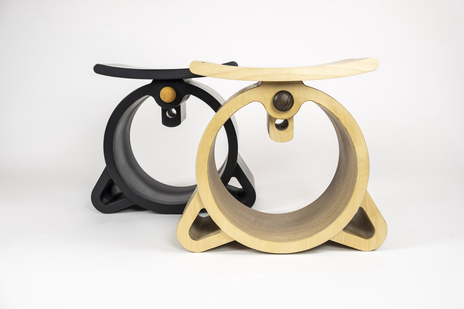 Two plywood stools, one blonde, one black. The bodies are big circles on their sides with short legs. Adjustable seat height.