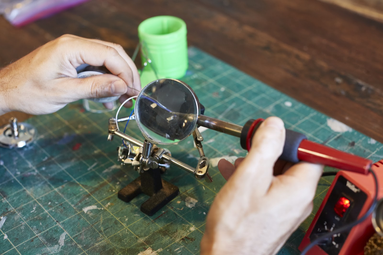 Closeup of someone soldering two wires together under a magnifying glass.