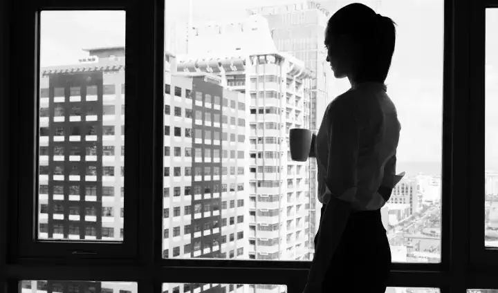 Black and white silhouette of a person with a ponytail against the bright background of a high-rise office window