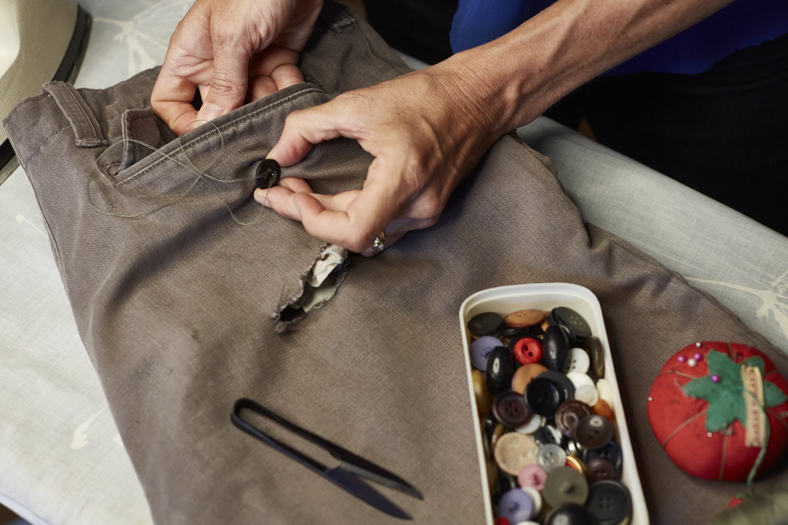 Closeup of someone using needle and thread to replace a button on the back pocket of a pair of pants.